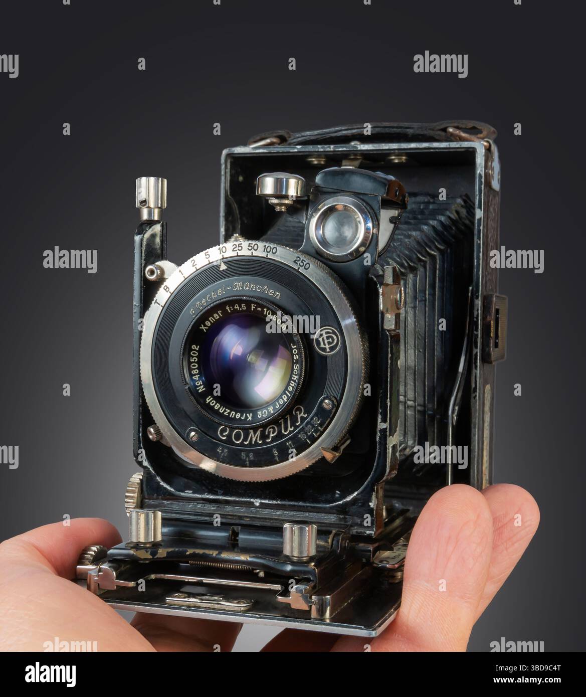 Una mano tiene in mano una fotocamera antica con un obiettivo dettagliato e un soffietto, che mette in risalto il suo design classico e il suo significato storico. Foto Stock