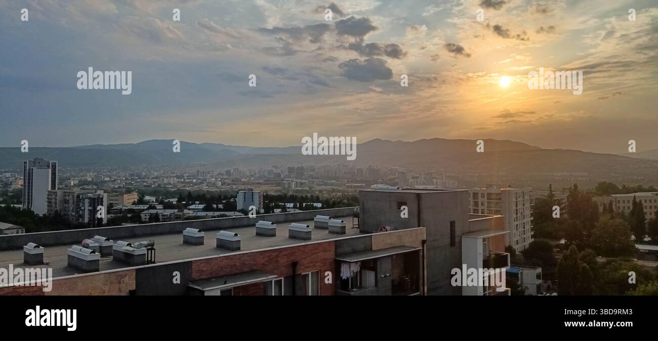 Tramonto panoramico su Tbilisi, Georgia, con una luce dorata soffusa che illumina lo skyline della città e le sagome delle montagne. Una fine pacifica e calda del Foto Stock