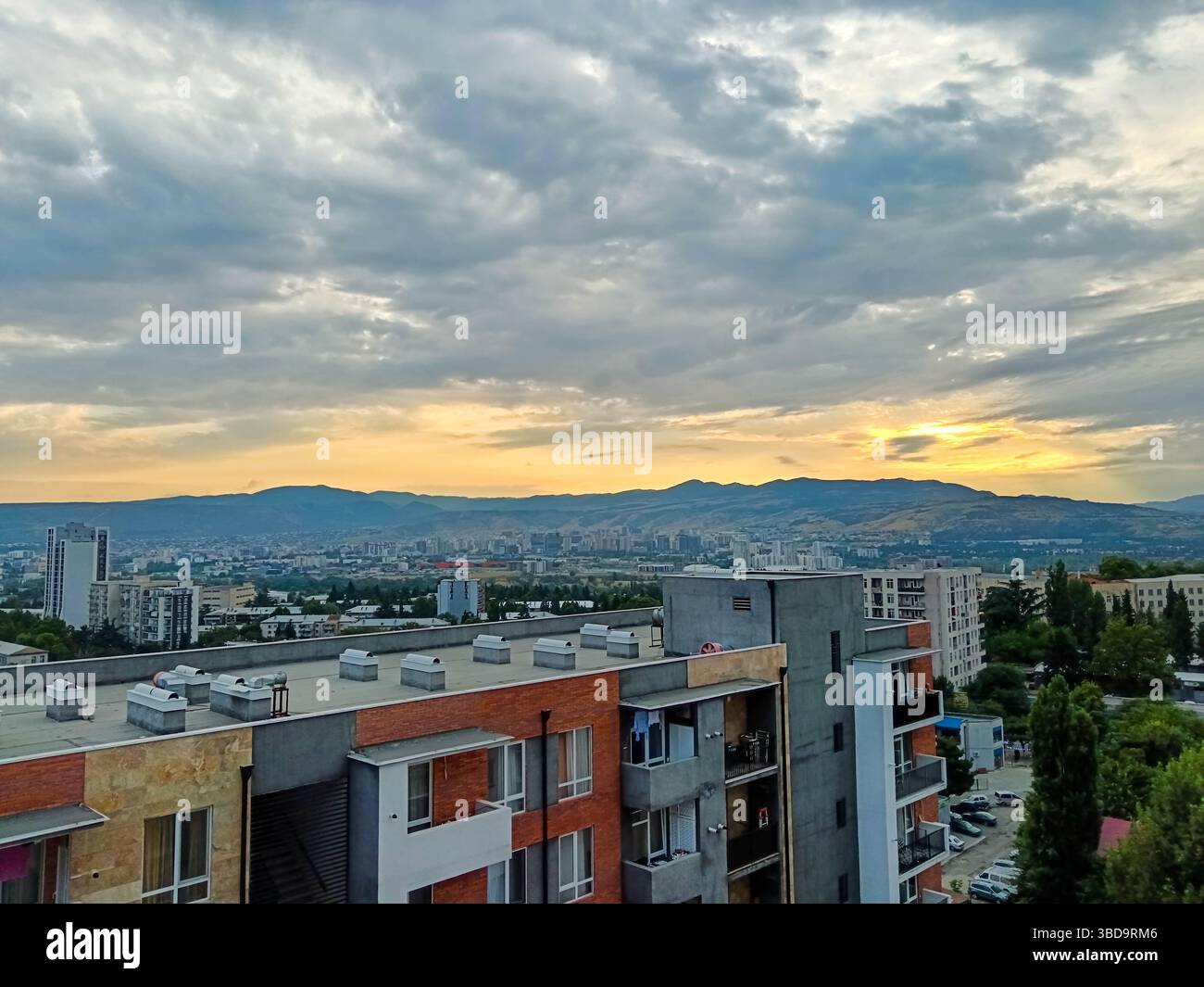 Tramonto panoramico su Tbilisi, Georgia, con una luce dorata soffusa che illumina lo skyline della città e le sagome delle montagne. Una fine pacifica e calda del Foto Stock