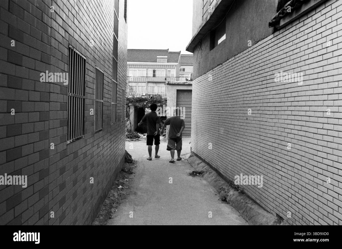 Due uomini che camminano attraverso uno stretto vicolo murato di mattoni nella Cina dei primi anni '2010 Foto Stock