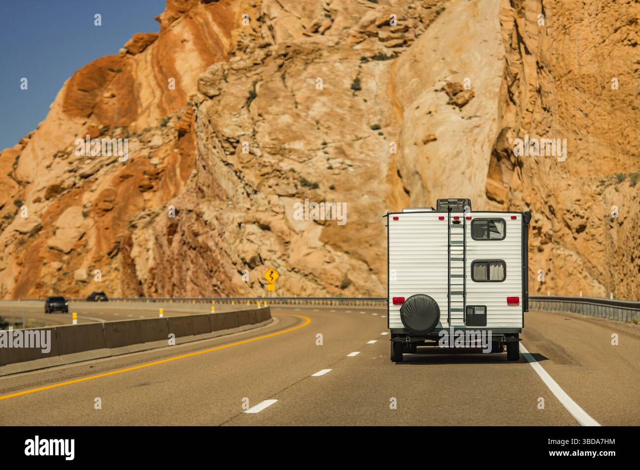 Un veicolo ricreativo guida lungo una strada tortuosa, fiancheggiata da torreggianti formazioni rocciose, sotto un cielo blu brillante in una giornata di sole. La bellezza della natura lo è Foto Stock