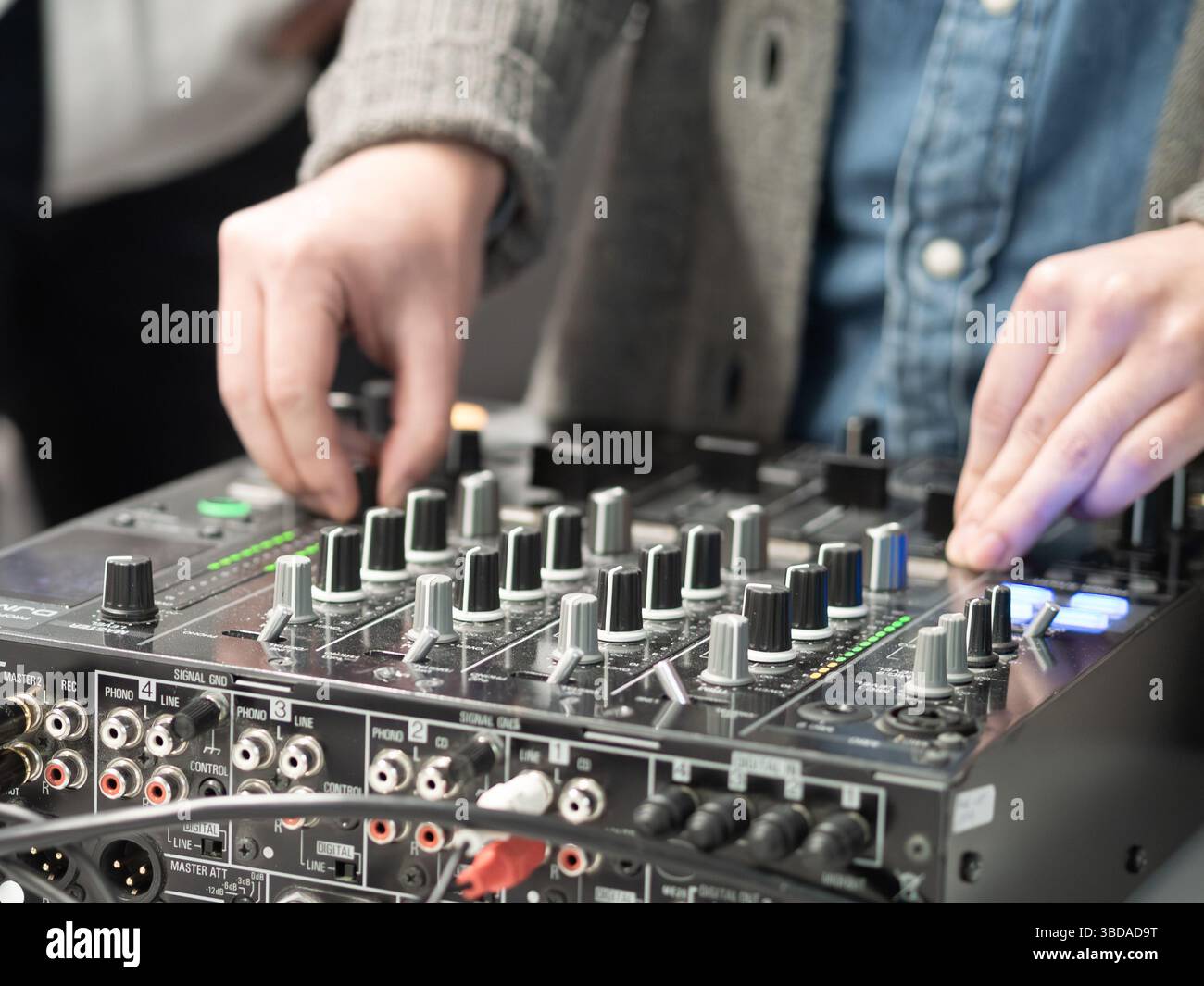 Un DJ gestisce sapientemente un mixer audio durante un evento musicale dal vivo. Luci colorate illuminano l'area, migliorando l'atmosfera energetica dei partecipanti Foto Stock