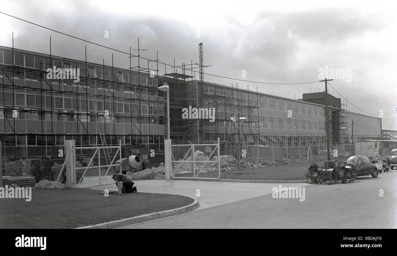 Anni '1960, storici, nuovi uffici su larga scala in costruzione in una zona industriale, Whitney, Oxford, Inghilterra, Regno Unito. Parcheggiato all'esterno da un capanno del Clerk of Works, vari veicoli a motore, tra cui un'auto a tre ruote, una motocicletta con sidecar, scooter e pedalate. Foto Stock