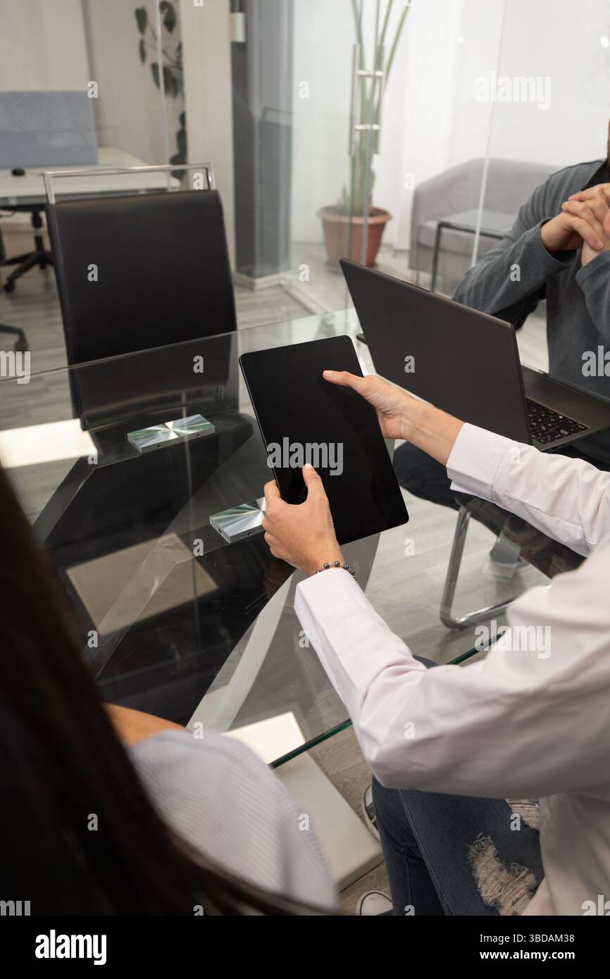 Una giovane donna si concentra sul suo tablet mentre è seduta a un tavolo, rappresentando tecnologia, connettività e uno stile di vita digitale moderno in un setti rilassato Foto Stock