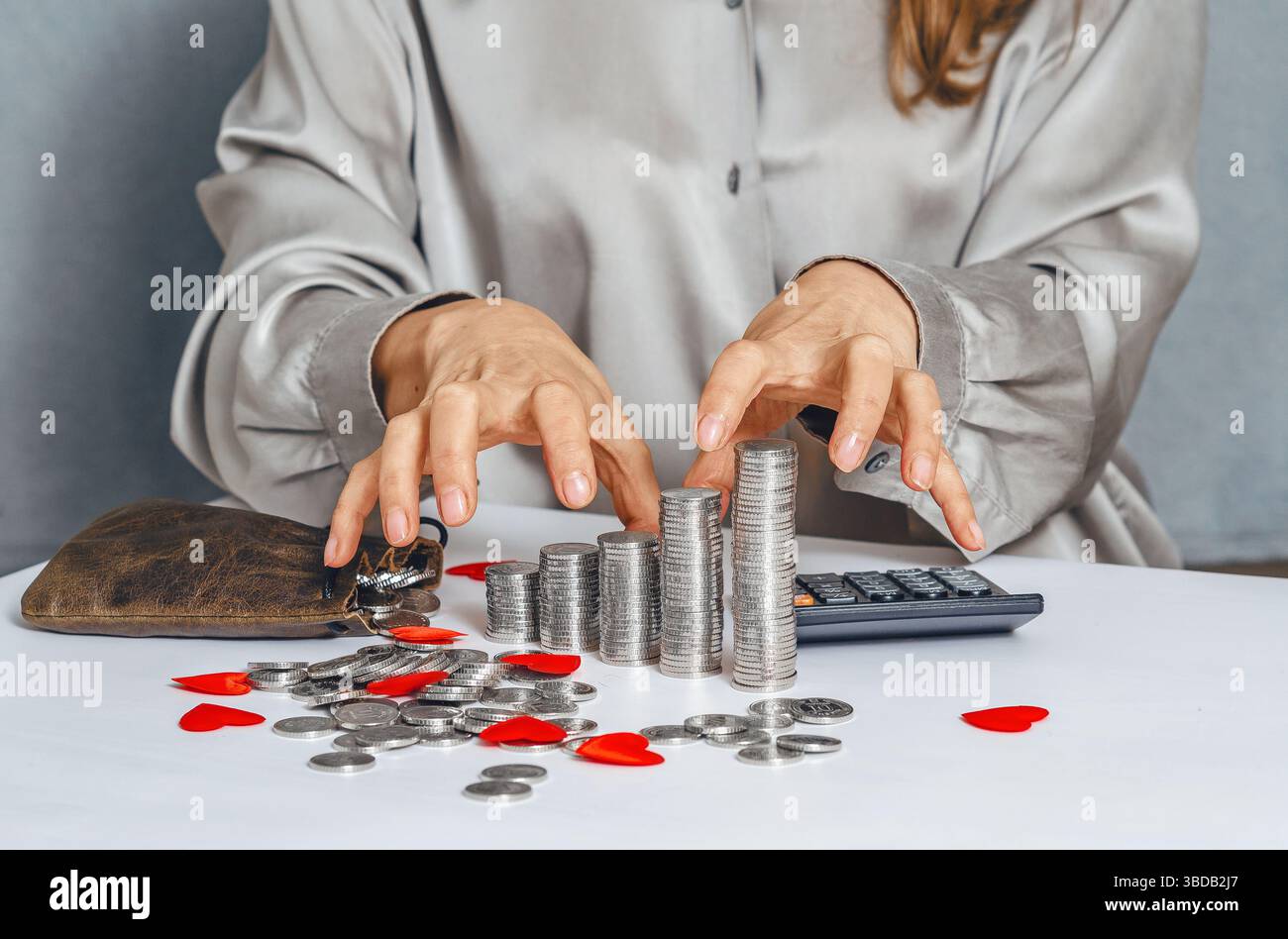 Avide mani femminili che raggiungono monete d'argento con cuore rosso. Borsa in pelle, calcolatrice. Concetto di furto, appropriazione indebita, frode e avidità Foto Stock