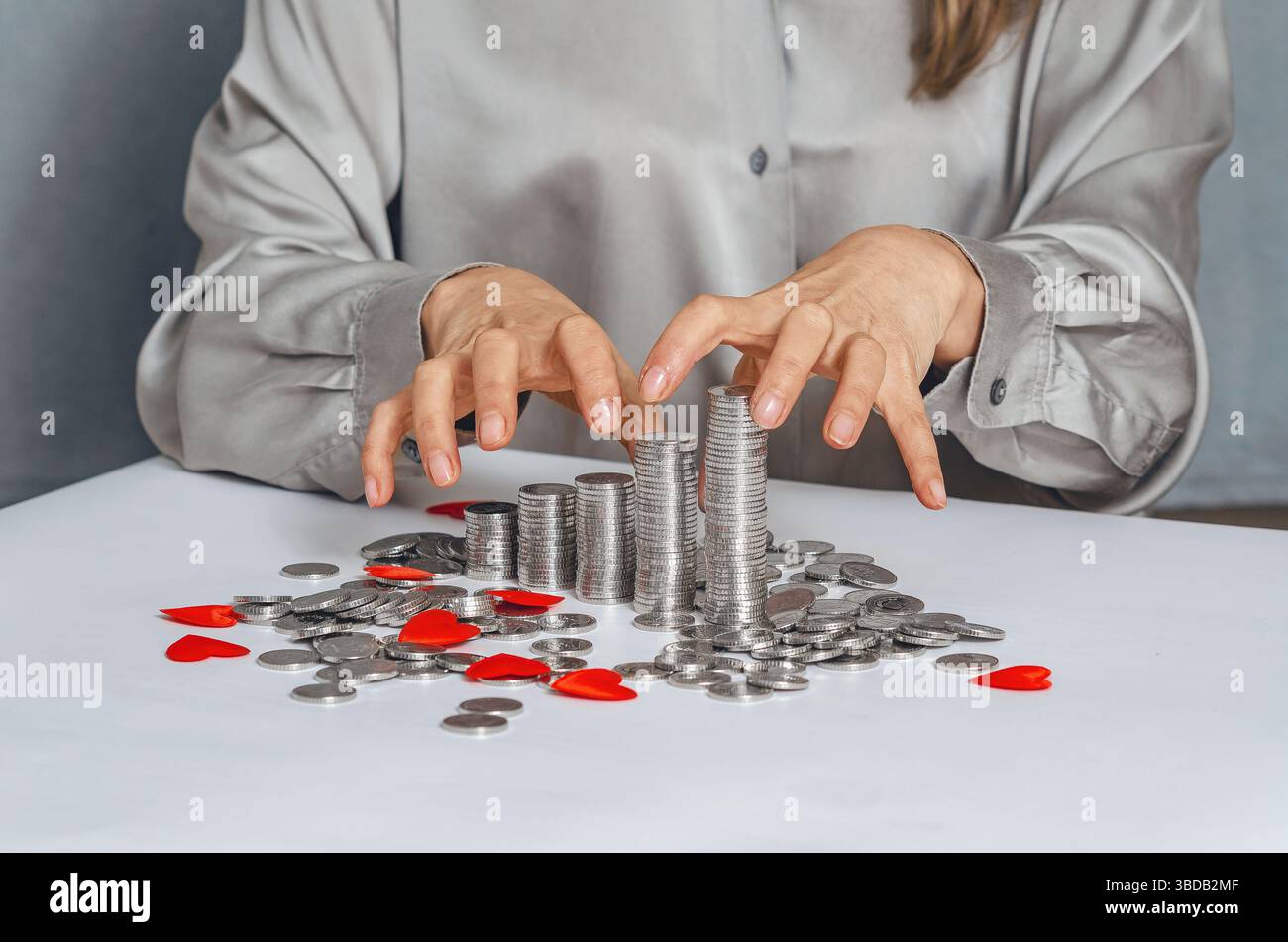 Mani avide che raggiungono pile di monete d'argento con cuore rosso. Primo piano di furti, appropriazione indebita, frode e avidità Foto Stock
