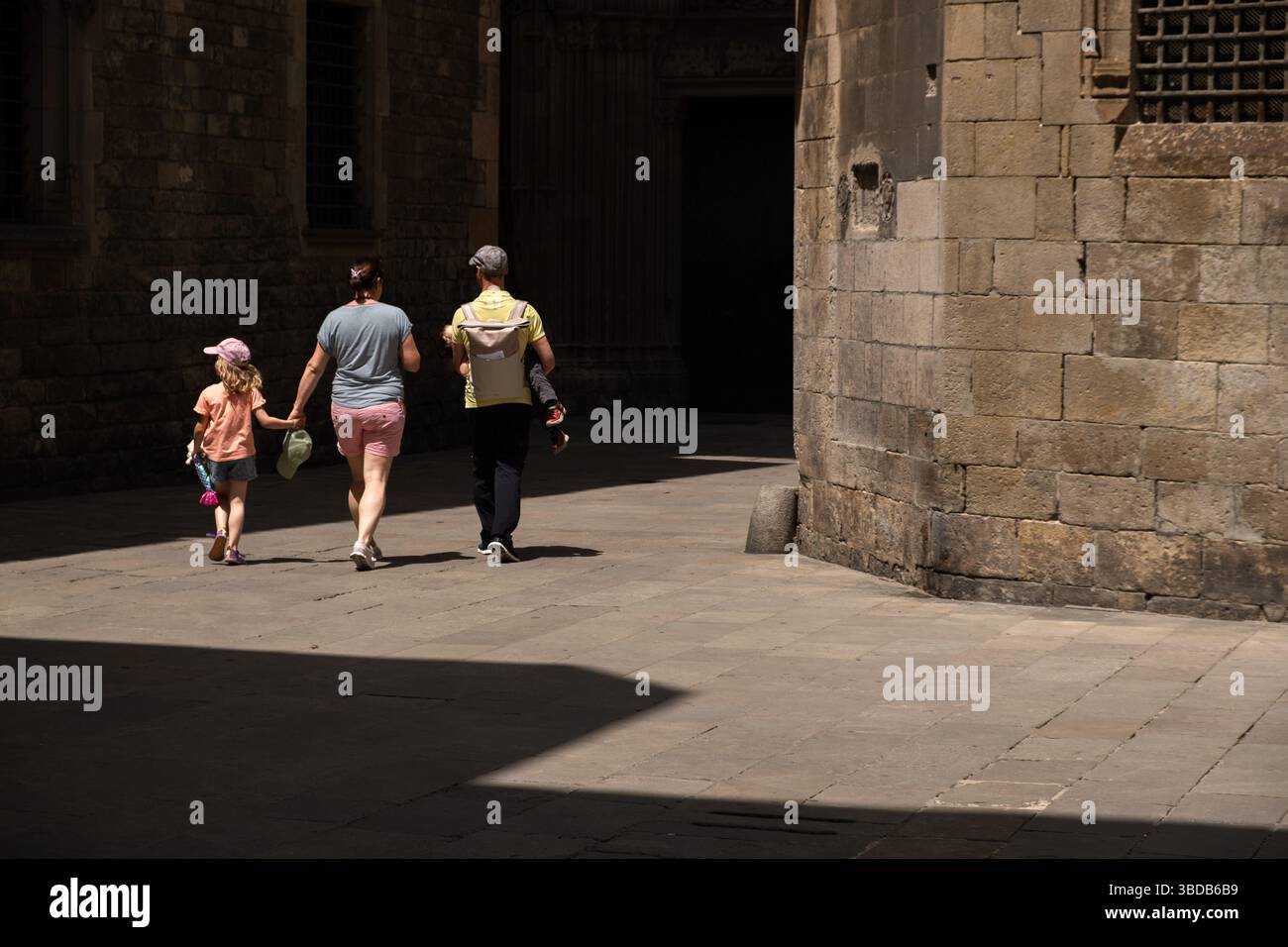 Una famiglia di turisti cammina attraverso i giardini monumentali della Cattedrale di Barcellona tra le luci e le ombre di mezzogiorno. Barcellona ha già un alto tasso di occupazione turistica con solo poche settimane di attesa fino all'arrivo dell'estate. Passeggiando per il quartiere medievale di Barcellona su un circuito ricco di intrattenimento culturale e fast food, la maggior parte della giornata è dedicata ai turisti di massa che visitano e amano la città. Foto Stock