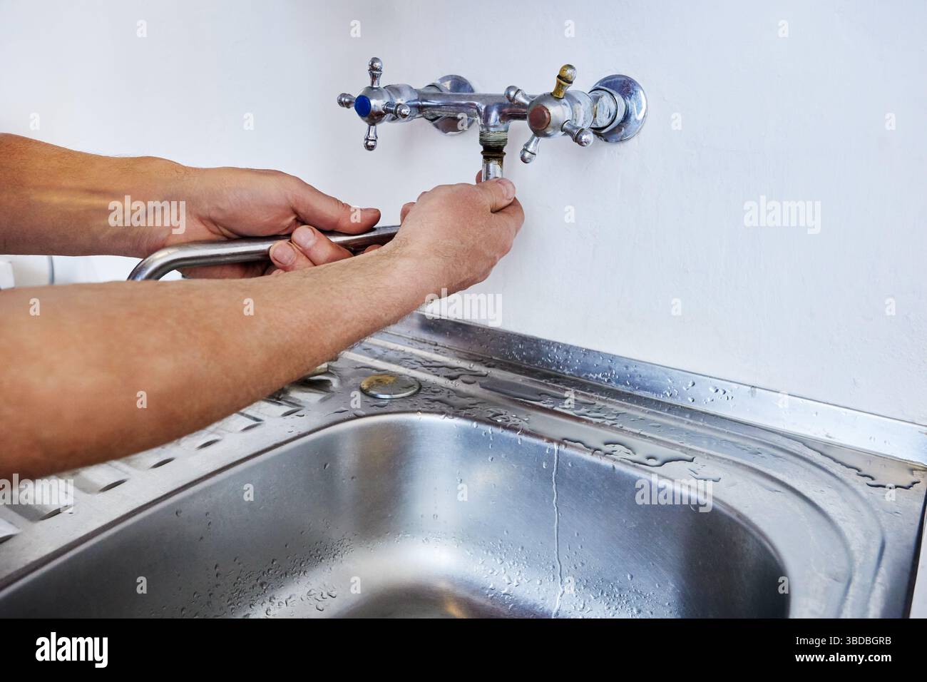 Man sta sostituendo il beccuccio del rubinetto montato a parete con le mani senza attrezzi, mentre le tracce d'acqua rimangono vicino al lavandino sul piano di appoggio in metallo. Foto Stock
