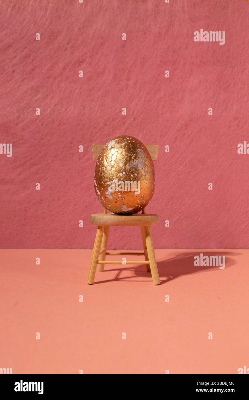 Uovo dorato su sedia di legno con sfondo rosa. Composizione minimalista Foto Stock