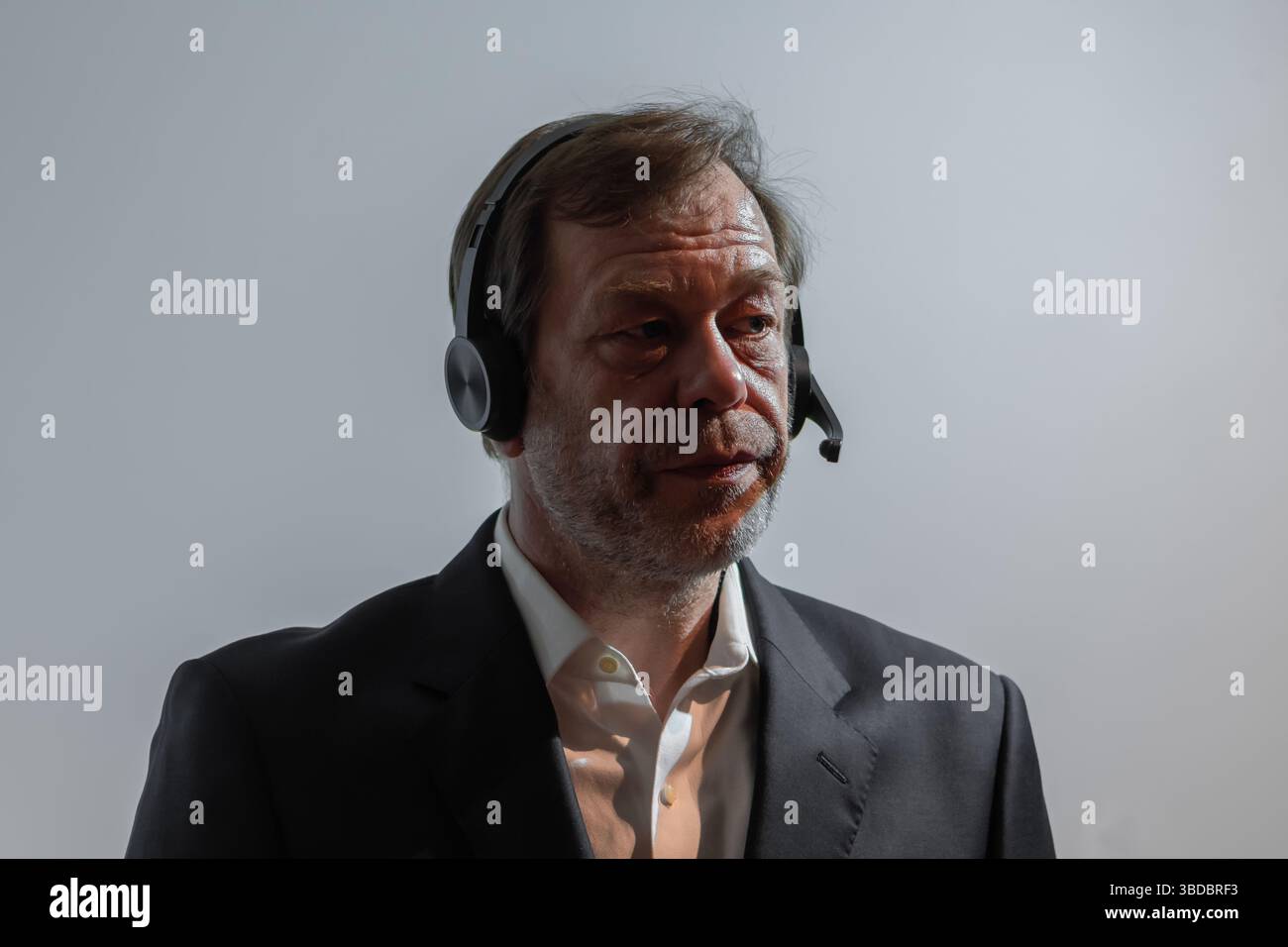 Uomo con tuta e cuffia con microfono contro una parete grigia. Un uomo di mezza età con un'espressione seria, che indossa un abito da lavoro, parla o li Foto Stock