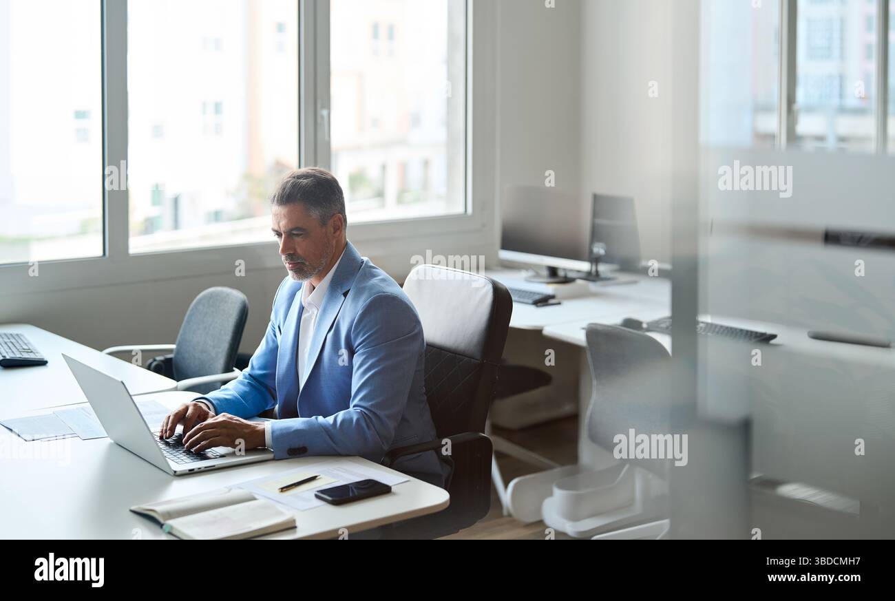 Un uomo d'affari anziano di mezza età impegnato che lavora su un computer portatile in ufficio. Foto Stock