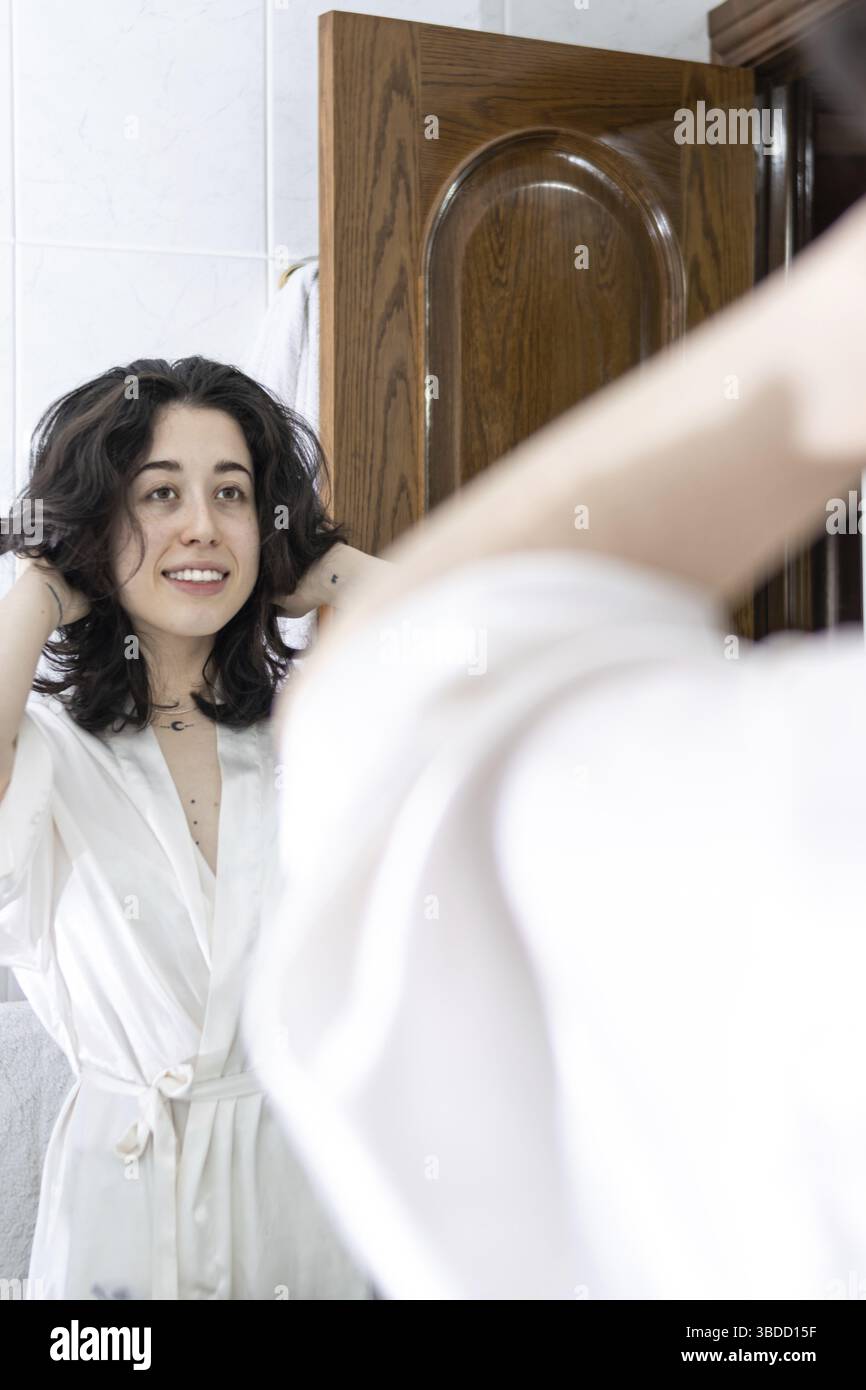 Donna felice in bagno. Giovane donna che gioca con i capelli davanti a uno specchio Foto Stock