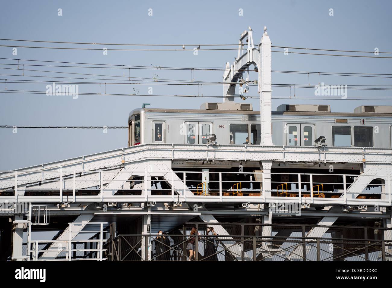 Asakusa, Tokyo, Giappone 03-23-2025: Treno e persone che attraversano il fiume sul ponte di Sumida River Walk nel Parco Sumida Foto Stock