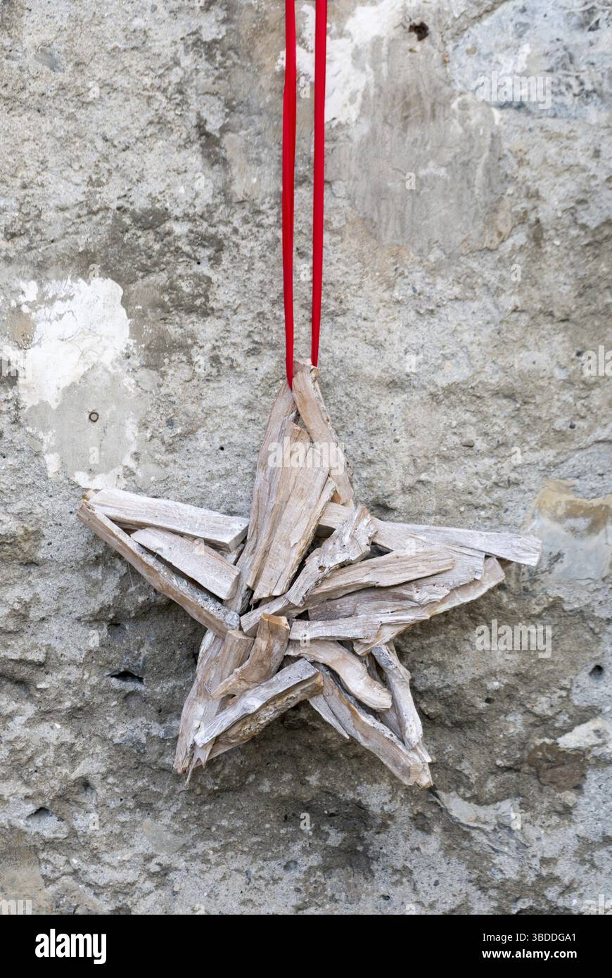 A forma di stella per accessori decorativi fatti a mano in legno appeso deon uno spesso filo rosso su una rustica roccia della parete anteriore della casa Foto Stock