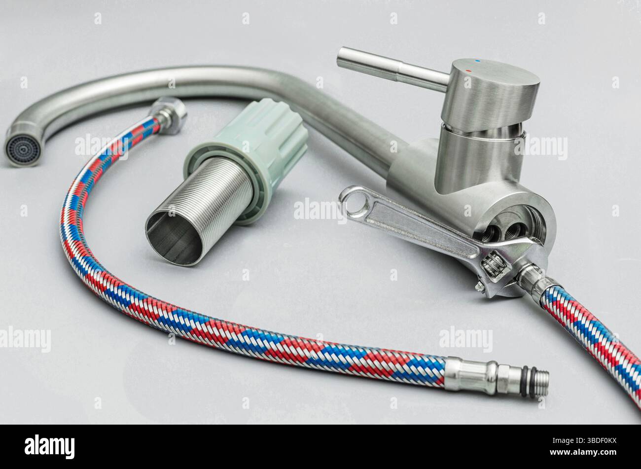 Primo piano di un nuovo rubinetto in acciaio inossidabile, tubi flessibili dell'acqua e una chiave regolabile, che rappresenta l'installazione di tubazioni, il miglioramento della casa o il rep Foto Stock