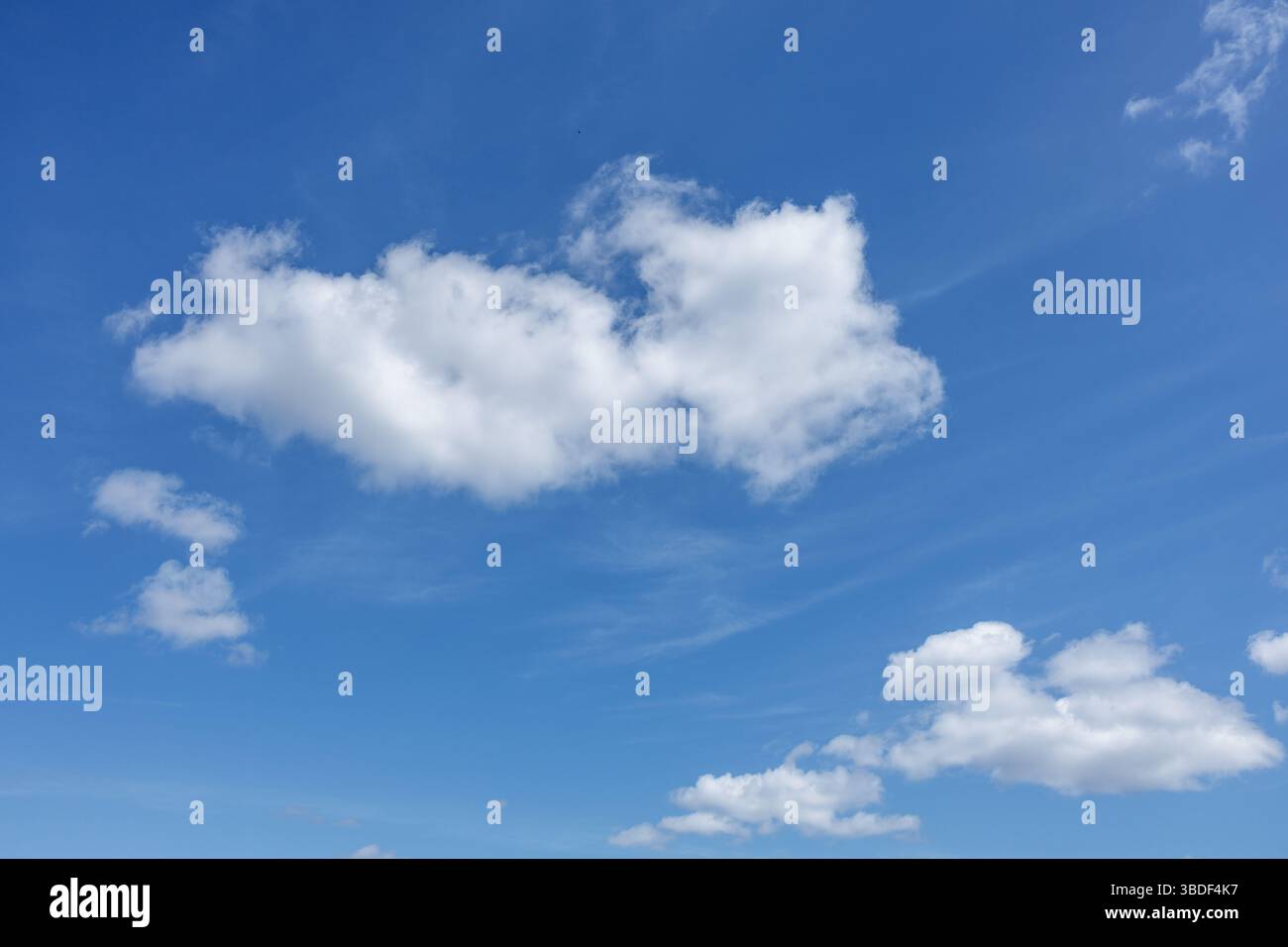 Grandi nuvole bianche e soffici attraversano il cielo azzurro in primo piano, creando un'atmosfera serena. Le tracce di fumetti in background aggiungono texture a Expanse. Foto Stock