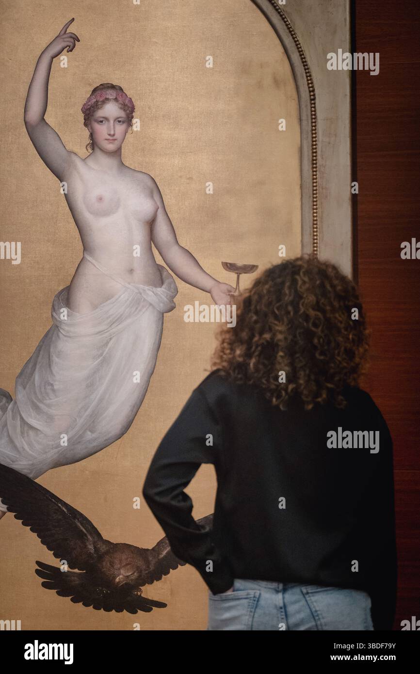 In questa immagine, vediamo una persona con i capelli ricci, che indossa una parte superiore di colore scuro e jeans di colore chiaro, in piedi di fronte a un dipinto. Il dipinto Foto Stock