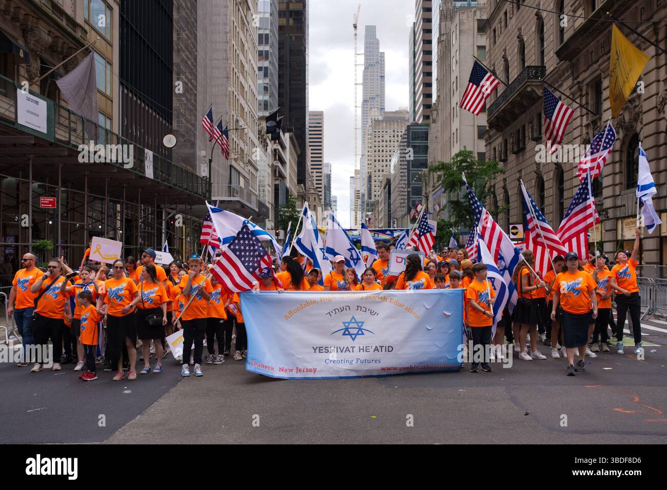 Un grande gruppo di persone, per lo più bambini e adulti che indossano camicie arancioni, marciano in una sfilata lungo una strada della città. Trasportano numerosi americani e ISR Foto Stock