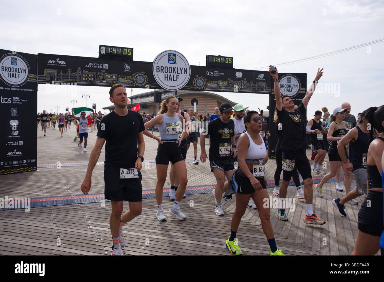 Corridori vicini al traguardo della Brooklyn Half Marathon. L'immagine mostra più corridori di diverse etnie ed età, indossando pettorali da gara, cros Foto Stock