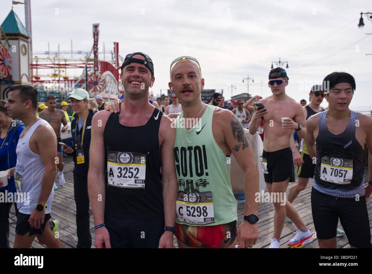 Due corridori maschi, uno nero e uno verde chiaro, stanno insieme a una gara. Indossano pettorali da gara e sorridono. Un'altra runne Foto Stock