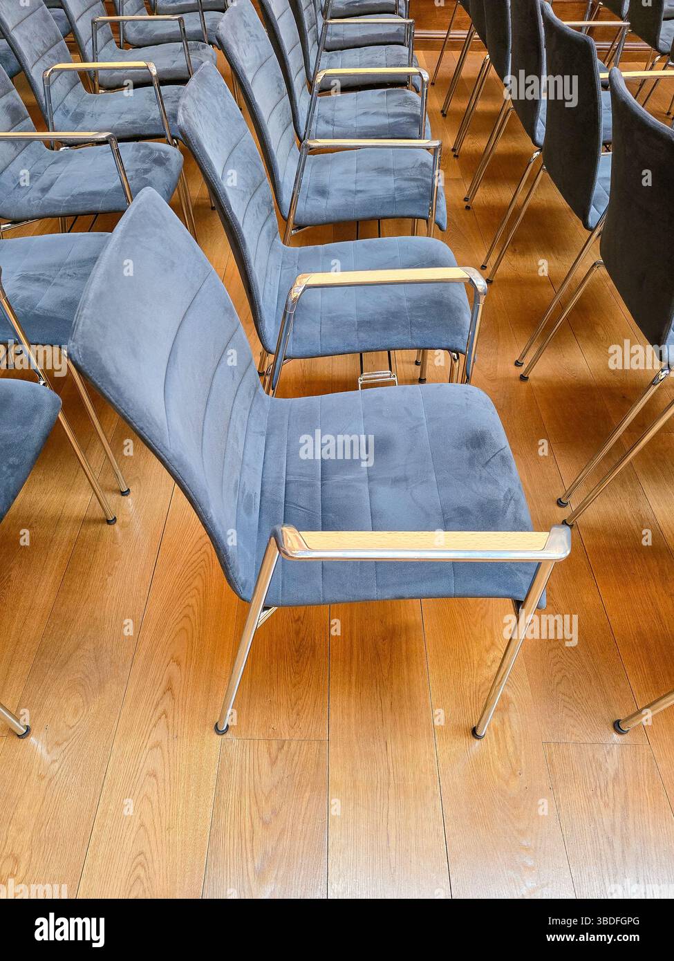 file di sedie blu identiche in una sala moderna con pavimento in legno, che evocano sottili disagi nell'uniformità Foto Stock