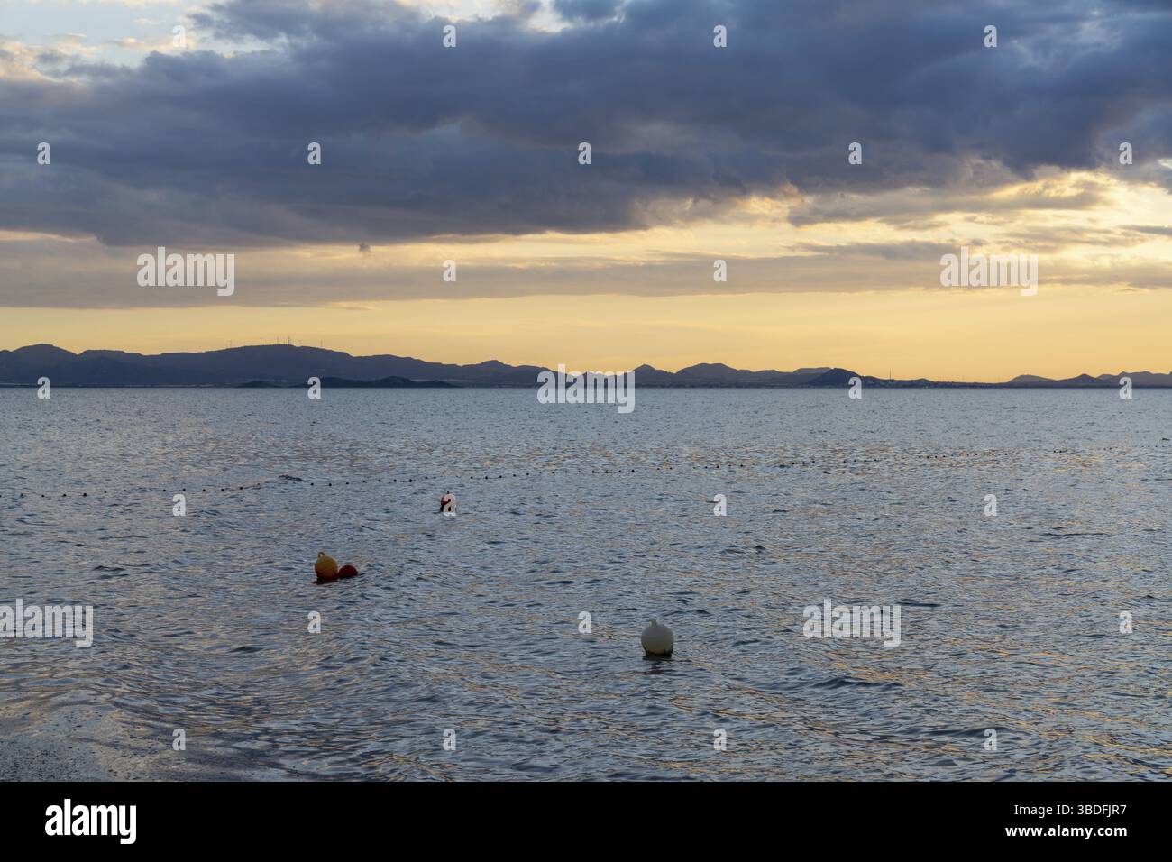 Vista delle calme acque oceaniche sotto un cielo espressivo a. tramonto con silhouette di montagna sullo sfondo e boe in il primo piano Foto Stock