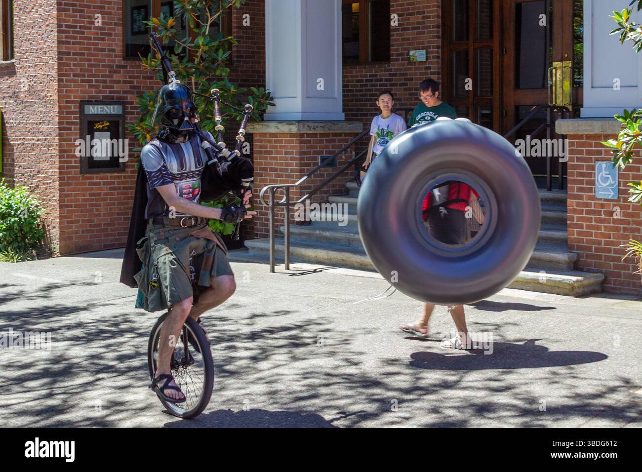 The Big Float, Portland, Oregon - 14 luglio 2018: Dart Fener su un unicicycle che gioca a cornamuse, mentre altri lanciano un gigantesco pneumatico gonfiabile. Foto Stock