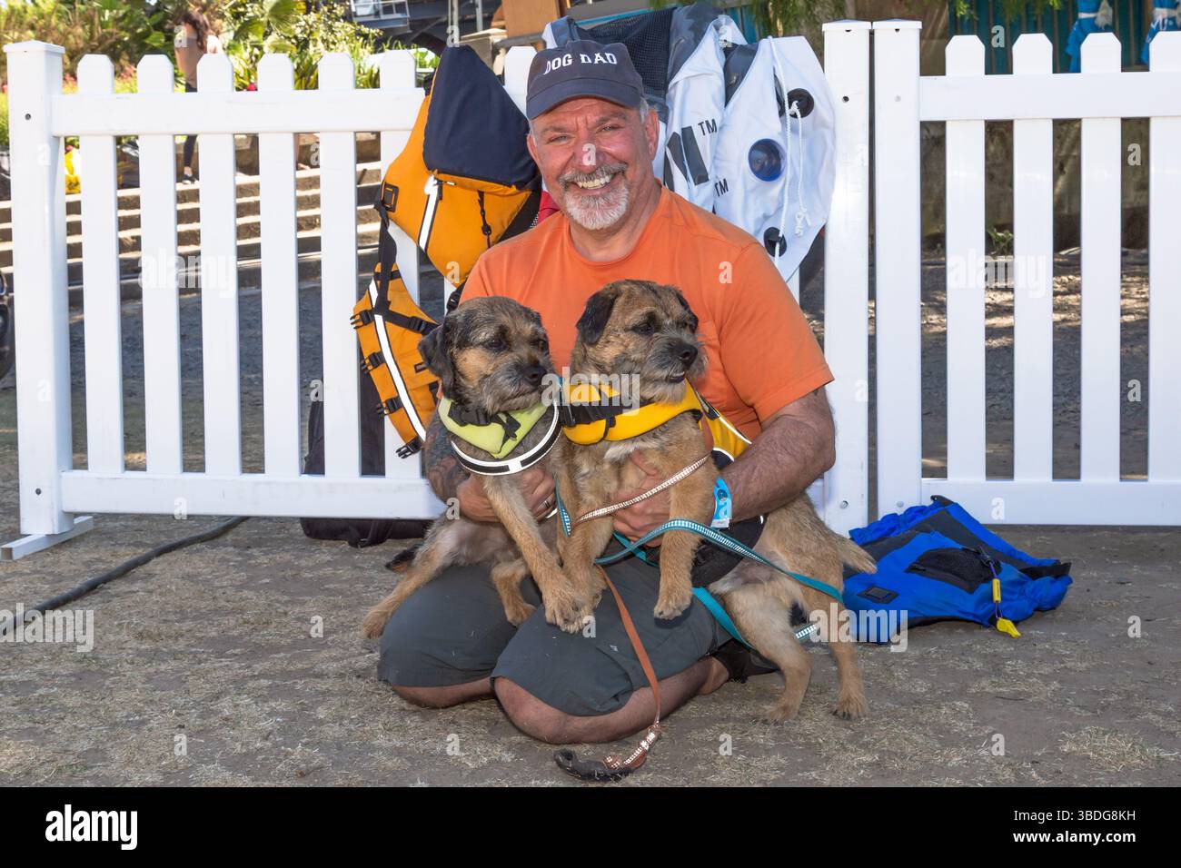 The Big Float, Portland, Oregon - 14 luglio 2018: Un uomo che indossa un cappello "Dog Dad" posa con due cani che indossano giubbotti salvagente, preparandosi per un galleggiante sul fiume. Foto Stock
