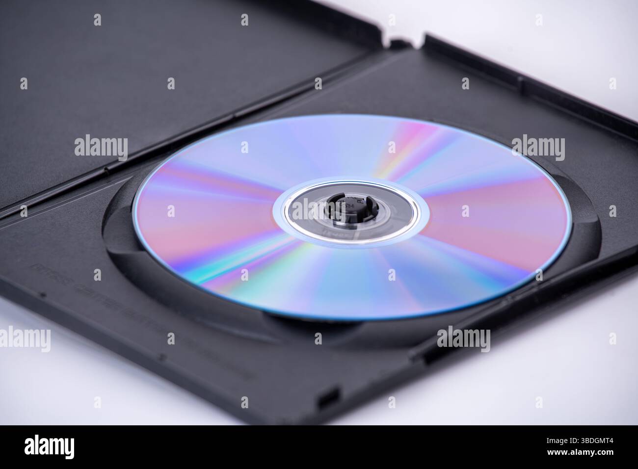 Un disco ottico con superficie riflettente è inserito all'interno di una custodia in plastica nera, parzialmente aperta, su sfondo bianco. il disco visualizza lo spettro dei colori Foto Stock