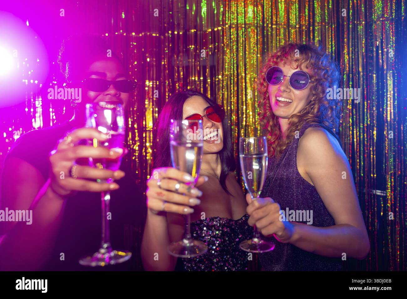 Tre donne multietniche stanno brinando con flute di champagne in un nightclub, godendosi la vivace vita notturna Foto Stock
