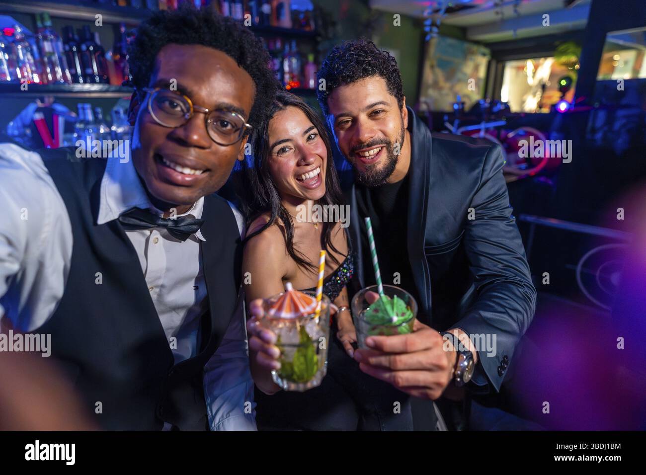 Allegri amici multietnici che scattano selfie e mostrano cocktail mentre si godono la vita notturna al nightclub bar Foto Stock