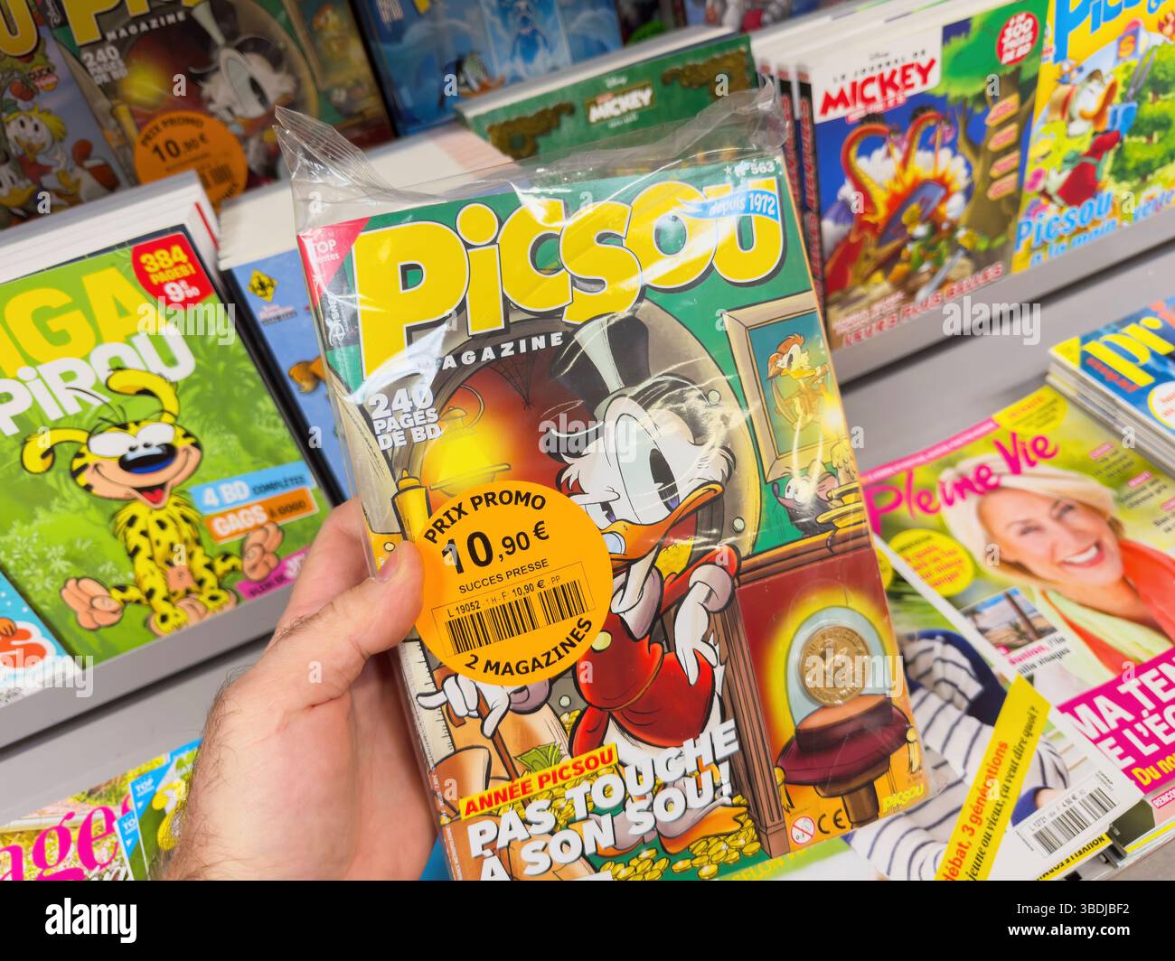 Parigi, Francia- 28 marzo 2025: Una mano regge una confezione doppia di Picsou Magazine con Scrooge McDuck sulla copertina con una moneta da collezione e un promo Foto Stock