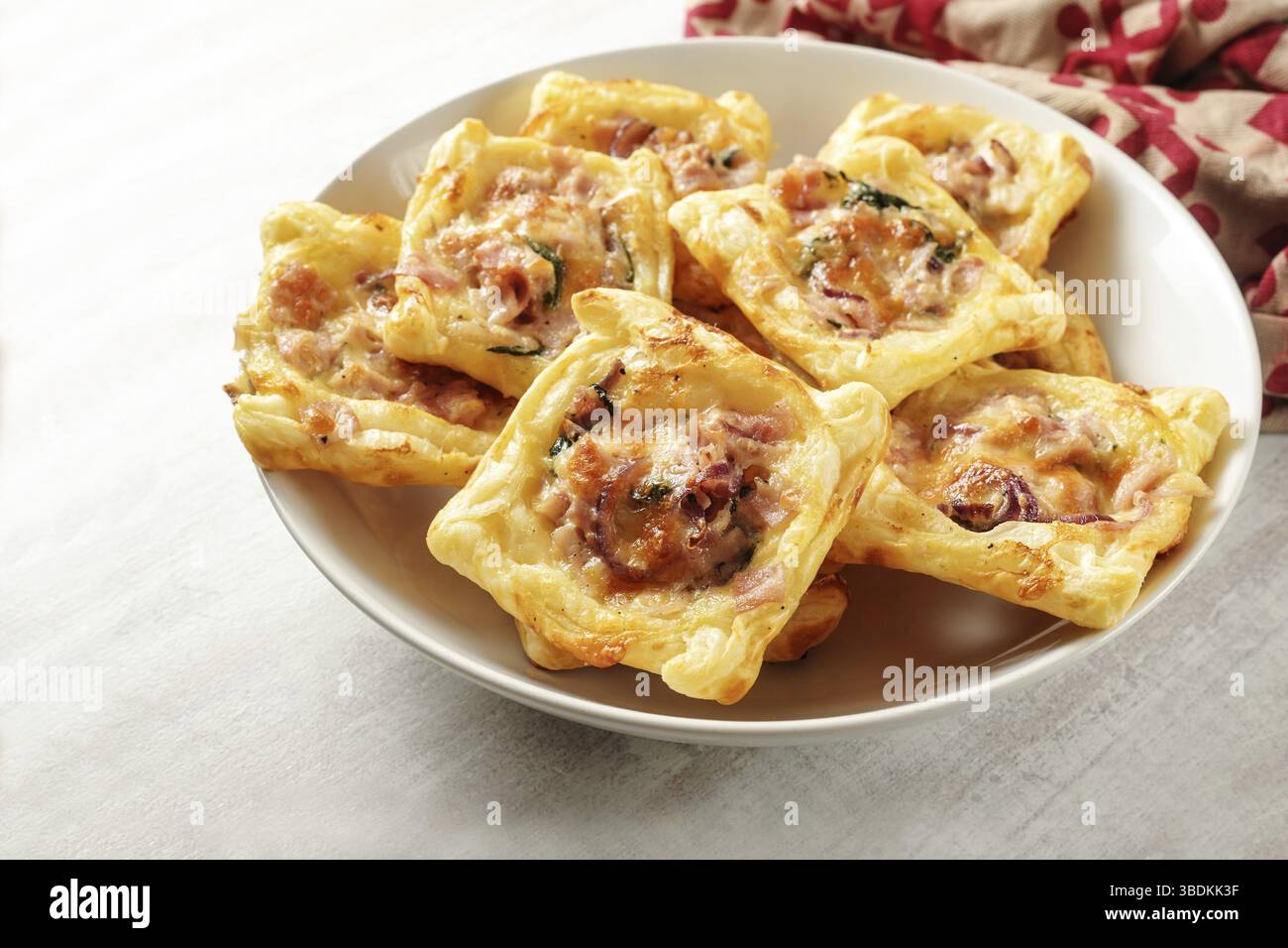 Quadrati di pasta sfoglia al forno con prosciutto, spinaci e formaggio in una ciotola bianca, snack finger food per una festa calda o fredda a buffet, spazio per fotocopie, focalizzazione selezionata Foto Stock