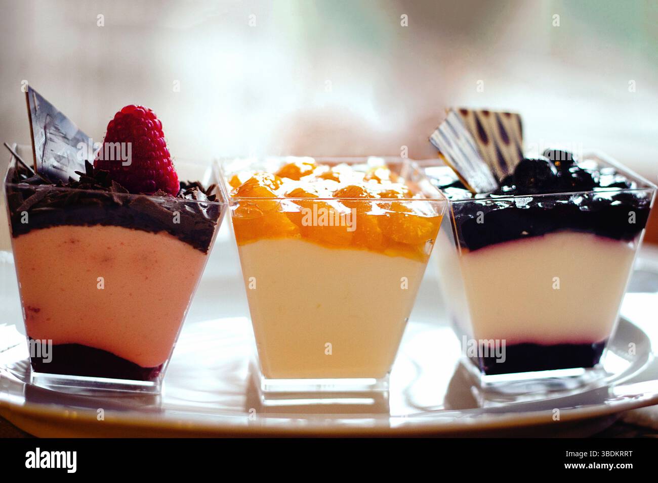 Primo piano del piatto con tre gustose cremose ricotta dessert in piedi nella fila con diverse deliziose marmellate di frutta e decorazioni al cioccolato. Foto Stock