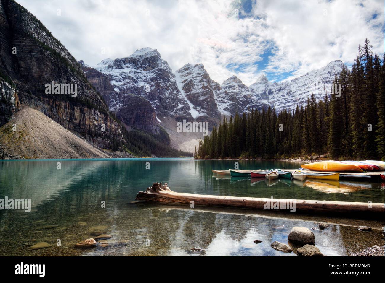 Canoe colorate riposano su un lago alpino cristallino con lo sfondo innevato delle montagne Foto Stock