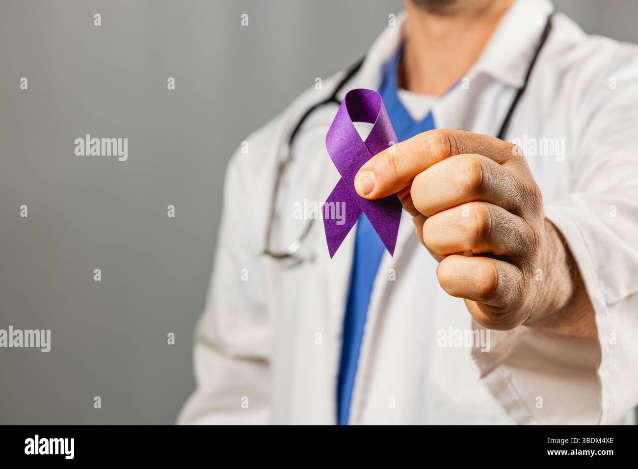 Un operatore sanitario in un cappotto bianco mostra un nastro viola, simboleggiando la consapevolezza. L'espressione focalizzata indica l'impegno per la causa della salute Foto Stock