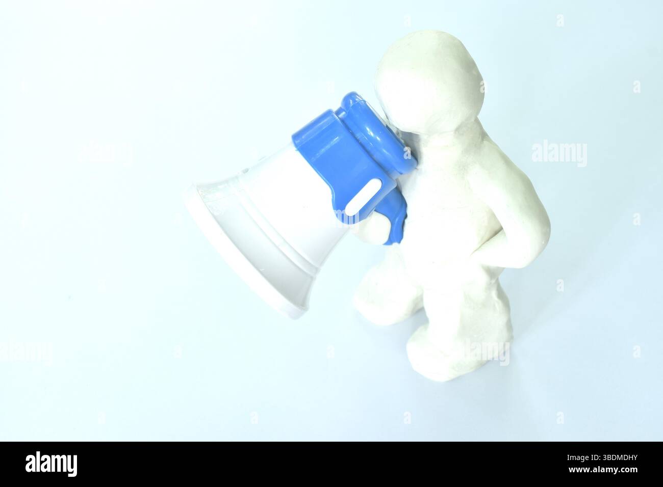 modello clay man che tiene in mano un megafono bianco e blu di plastica giocattolo e parla su sfondo bianco Foto Stock