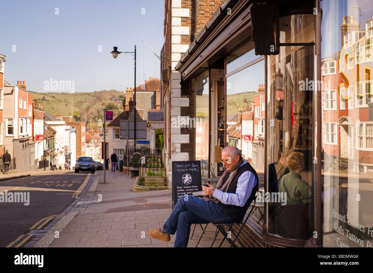 Un uomo anziano che guarda il telefono mentre si siede fuori da un bar a Lewes Foto Stock