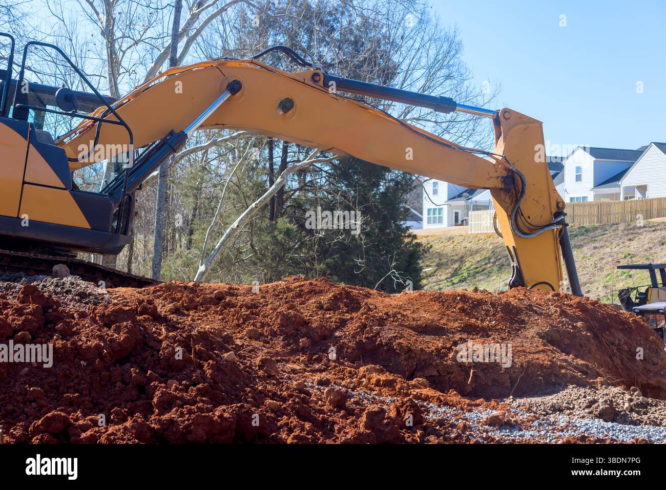 I macchinari pesanti eseguono gli scavi in cantiere poiché le case si affacciano sull'area di lavoro Foto Stock