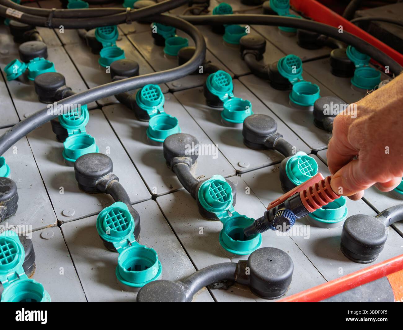 Eseguire manualmente la manutenzione delle celle industriali delle batterie al piombo con un utensile di riempimento dell'acqua. Foto Stock