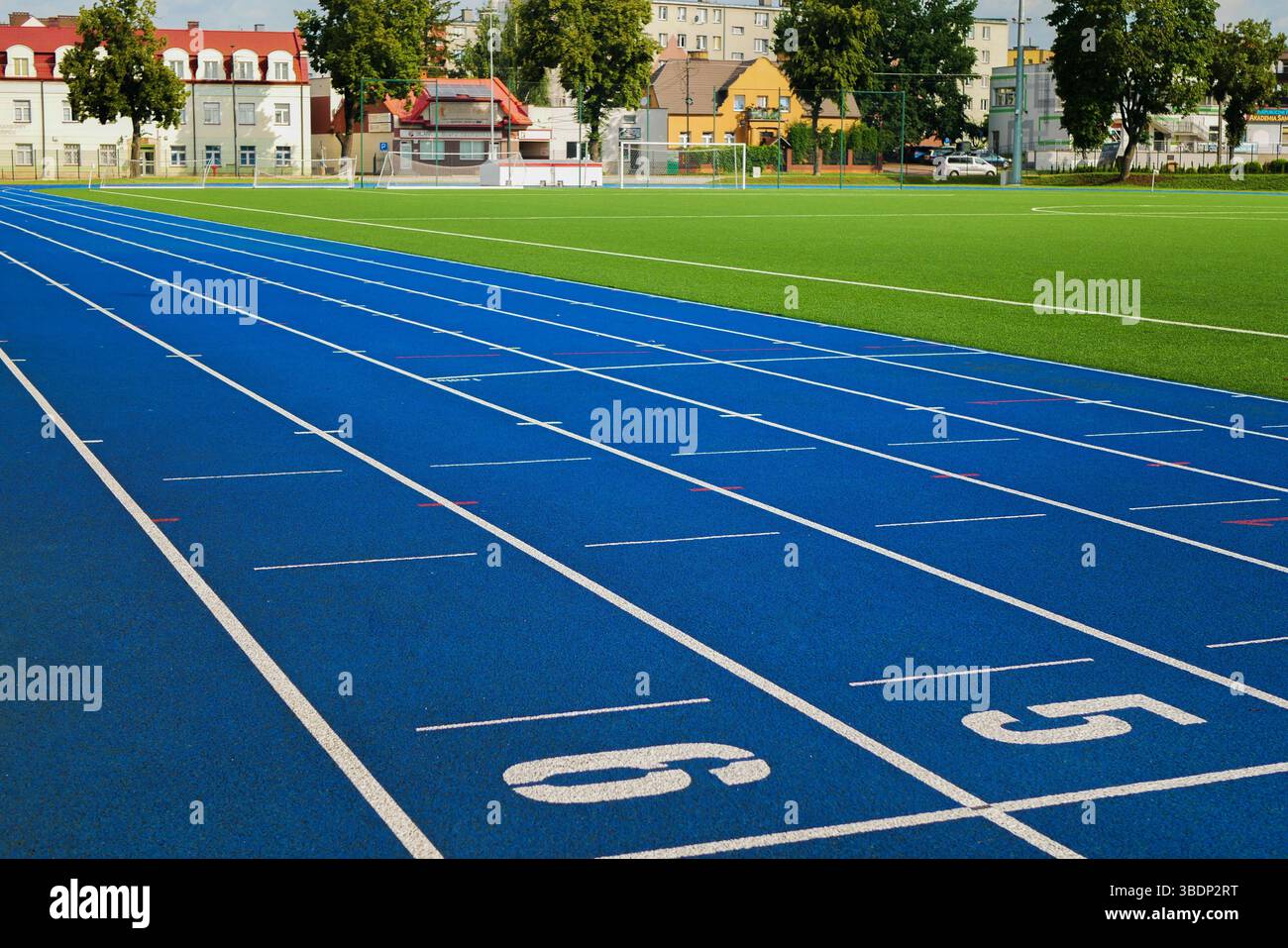 Moderna pista da running blu e campo da calcio verde in una zona urbana in una giornata di sole. Complesso sportivo all'aperto con corsie e numeri. Foto Stock