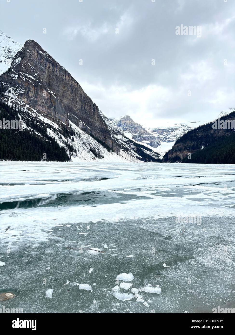 Il Lago Louise ghiacciato è circondato da montagne innevate sotto un cielo invernale nuvoloso, situato nel Parco Nazionale di Banff, Alberta, Canada. Foto Stock