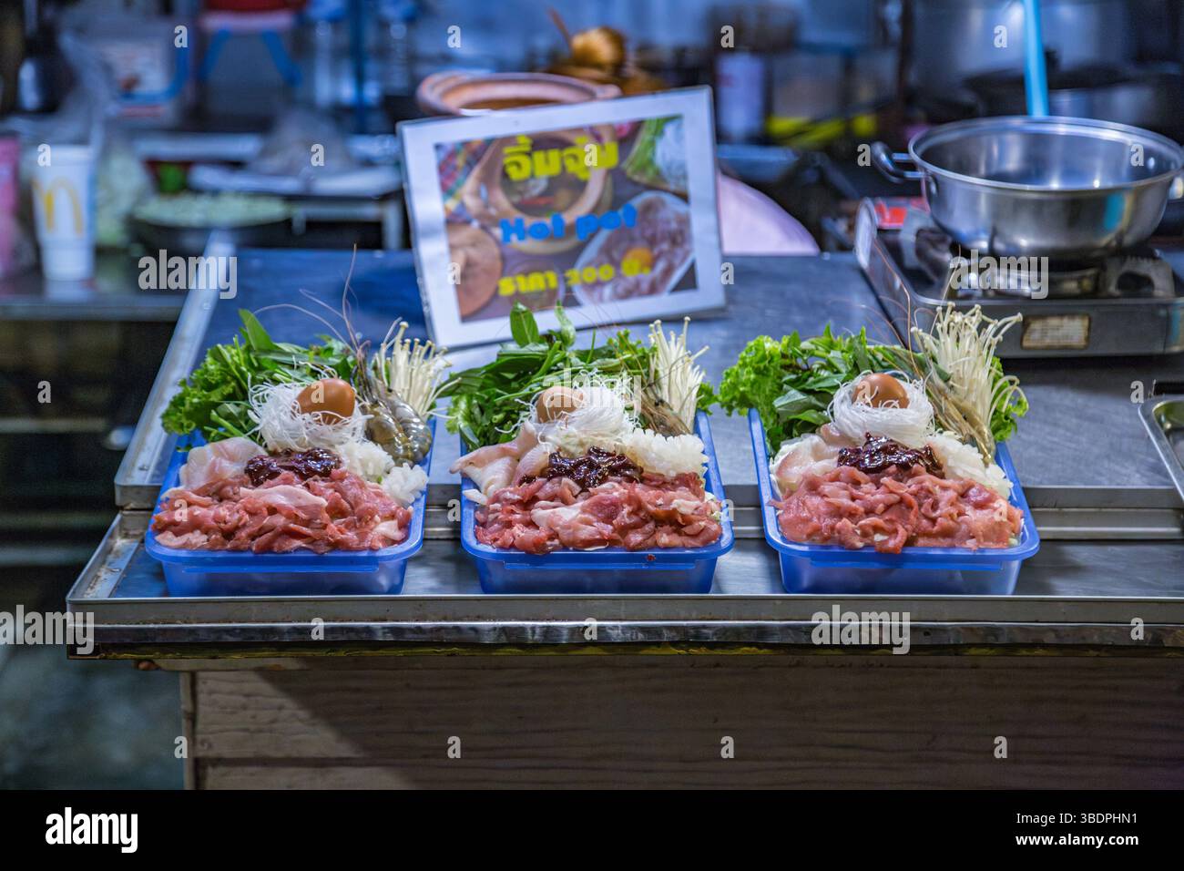 Il venditore thailandese di strada offre un pacchetto di pasti caldi che i clienti possono cucinare su un piatto caldo al loro tavolo al mercato notturno nel centro di Chiang Rai, Thailandia Foto Stock