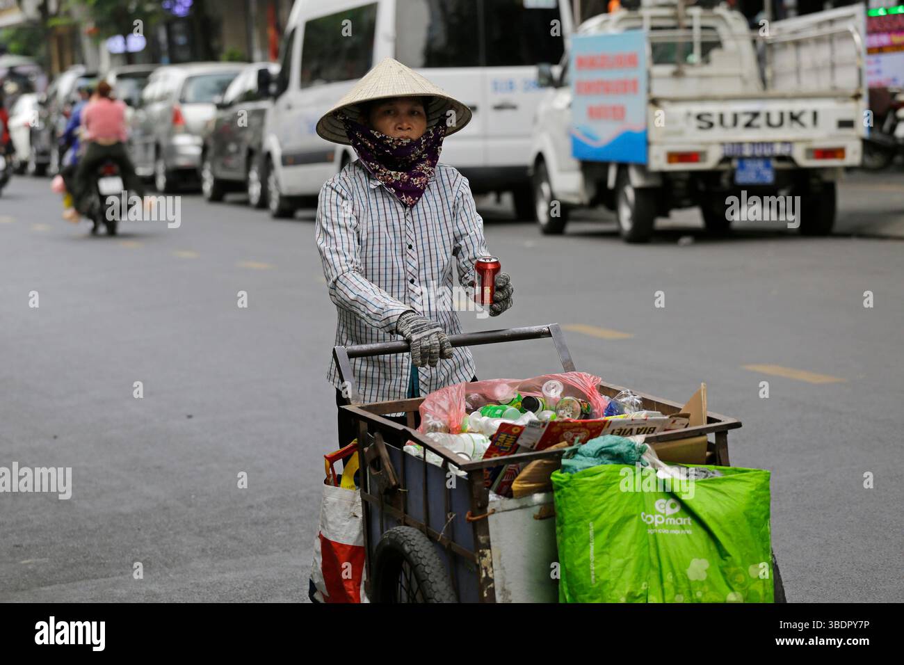 Ho chi Minh, Vietnam - 26 dicembre 2022: Donna vietnamita, che indossa un tradizionale cappello conico, non la, tira un carrello che trasporta merci per il riciclaggio. Foto Stock