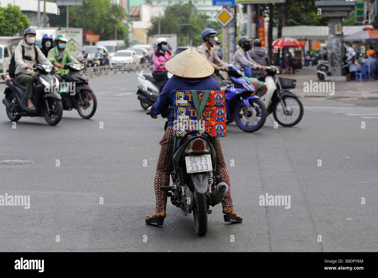 Ho chi Minh, Vietnam - 26 dicembre 2022: Donna vietnamita guida la sua moto indossando un cappello conico, non la, mentre trasporta birre Tiger. Foto Stock