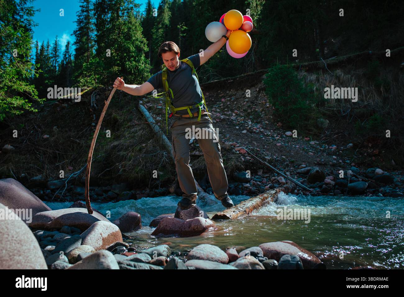 Uomo escursionista con palloncini attraversa il fiume turbolento in montagna Foto Stock