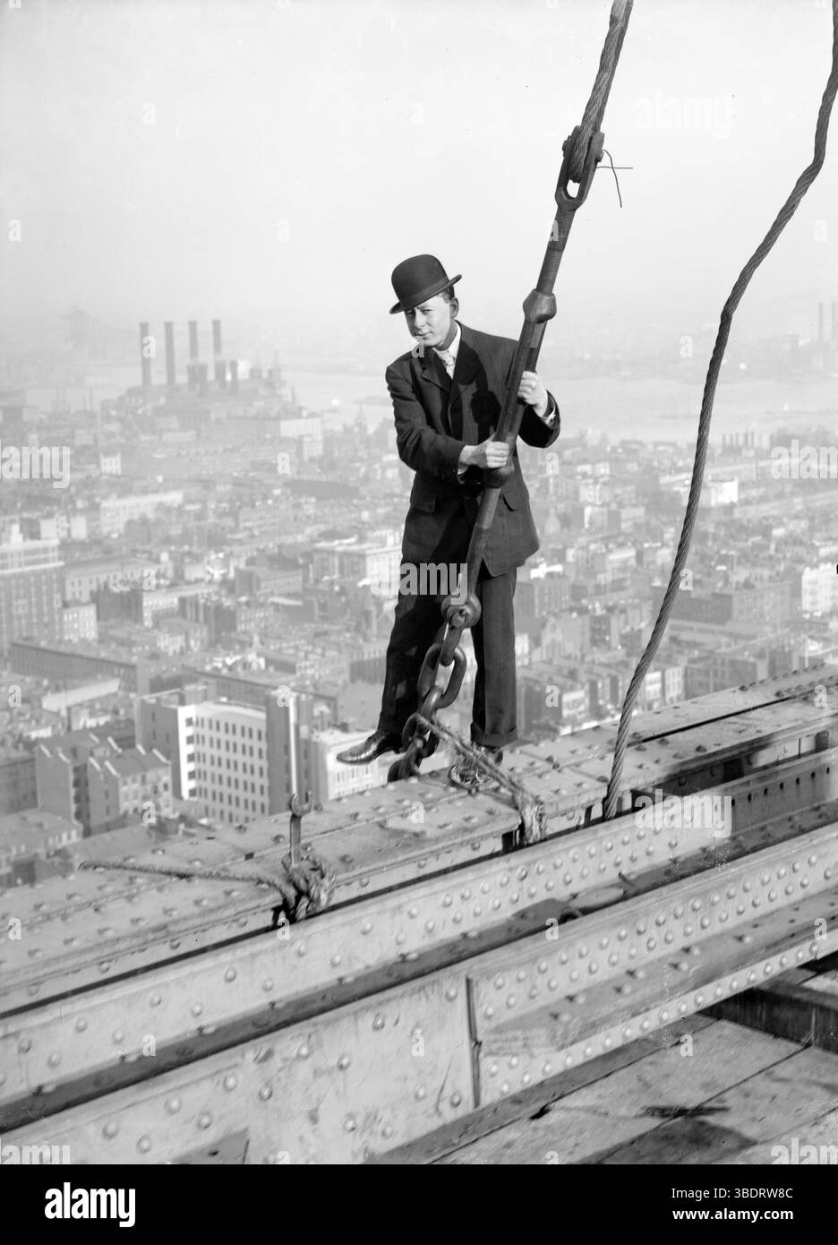 Un uomo con un abito e un cappello da bowler si erge su travi di ferro al 33° piano del Met Building, affacciato su Manhattan, New York, America Foto Stock