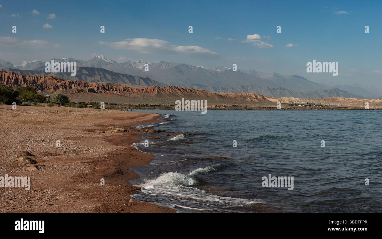 Spiaggia di sabbia rossa e montagne panoramiche sulla riva del lago Issyk-Kul in una giornata di sole Foto Stock