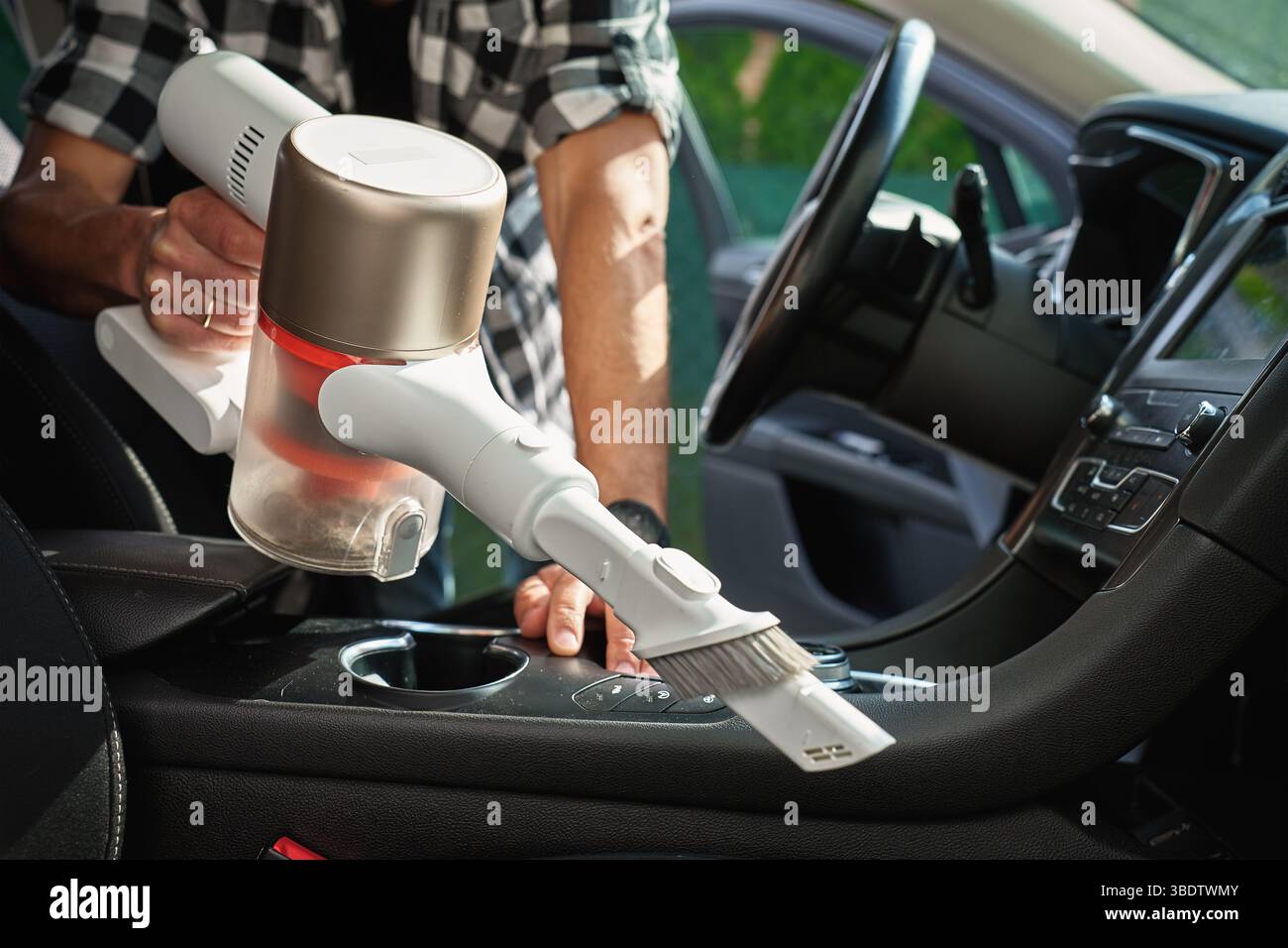 Man sta aspirando gli interni sporchi dell'auto con un aspirapolvere cordless portatile. Il proprietario dell'auto si prende cura del veicolo, della pulizia della tappezzeria del sedile e degli interni. Vehi Foto Stock