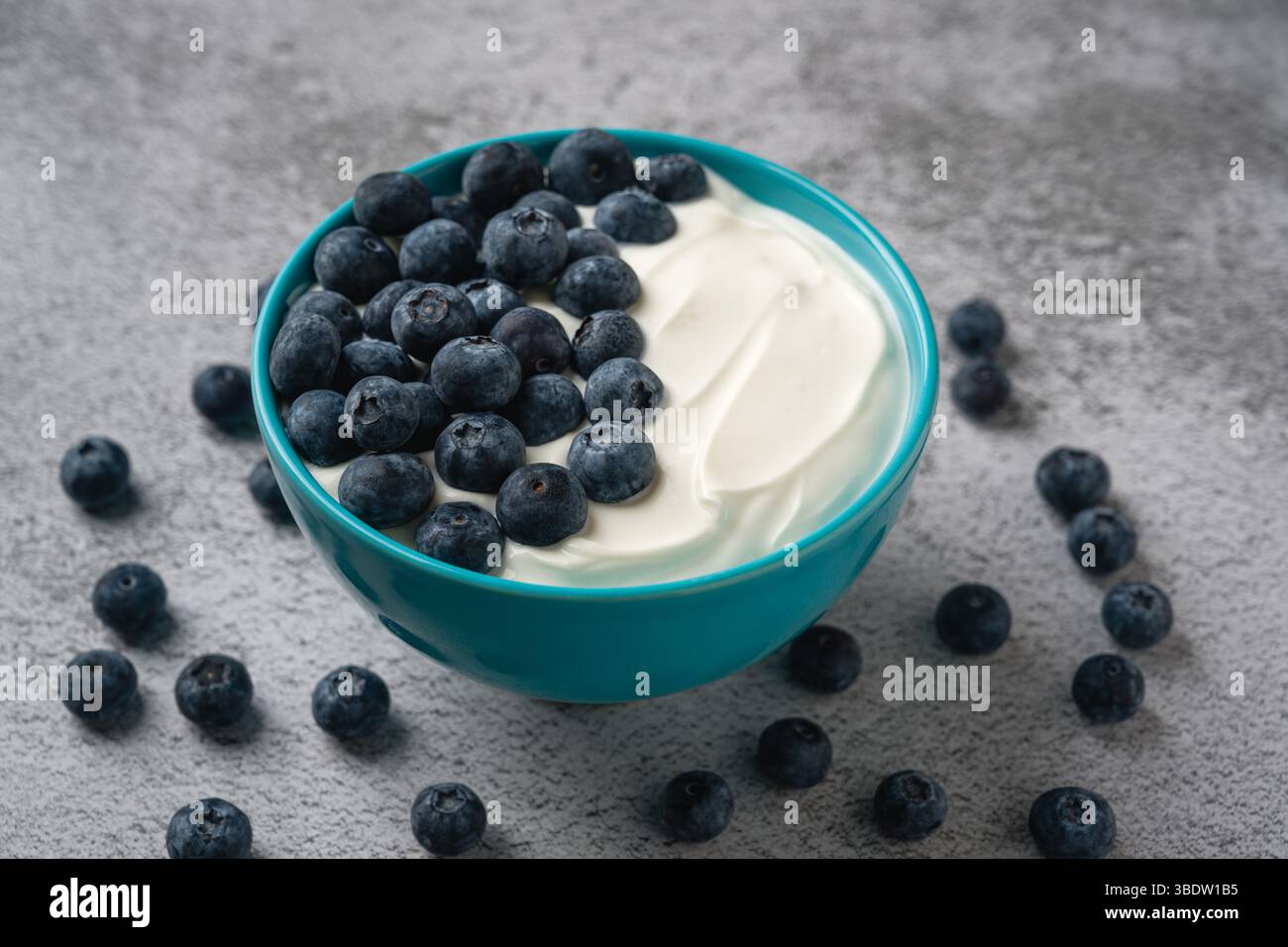 Vista dall'alto dei mirtilli freschi su uno yogurt cremoso in una ciotola blu Foto Stock